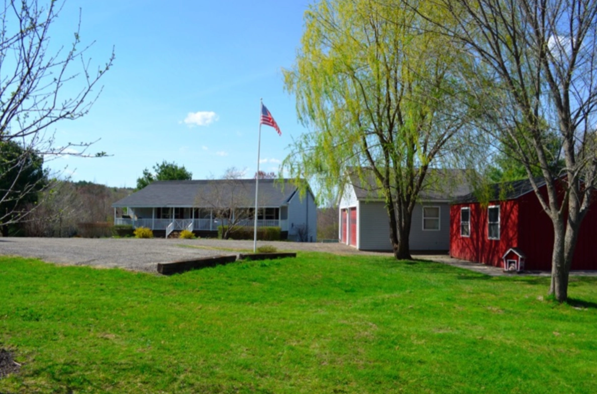 Red house, American flag, tree, green lawn.